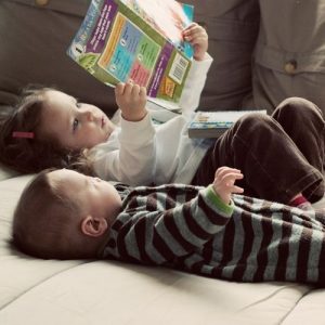 Image of two small children laying on their backs reading a book.