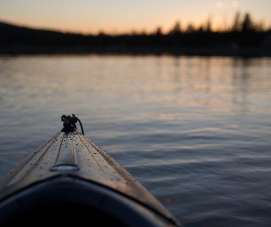 image of the tip of a canoe looking out on a dark lake. the shoreline is far away.