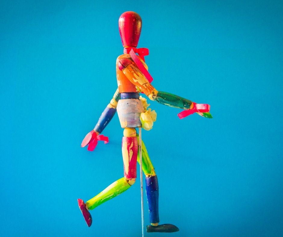 Image description is of a wooden model doll painted vibrantly. Backgraound is blue.